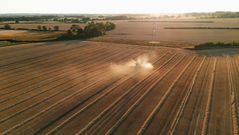 establishing drone shot of combine harvester in orange dust into the sun at golden hour sunset