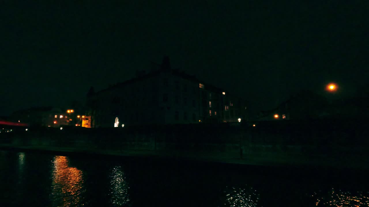 Le luci della città brillano nell'oscurità riflettendosi sulla superficie del fiume. Gli edifici fiancheggiano la riva del fiume sotto il cielo notturno, creando un'atmosfera vivace.