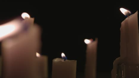 An-extreme-close-up-and-pan-across-of-white-candles-lit-with-a-black-background