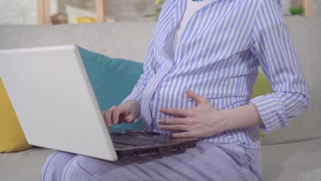 인식할 수 없는 젊은 임신한 여성이 노트북을 사용하여 인터넷을 검색합니다.