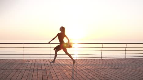 Bailarina-Con-Tutú-De-Ballet-Negro-Y-Punto-En-El-Terraplén-Sobre-El-Océano-O-El-Mar-Al-Amanecer.-Bailarina-Saltadora,-Practicando-Ejercicios-Clásicos.-Camara-Lenta