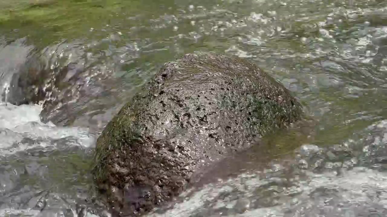 Air jernih mengalir di sekitar batu sungai besar.