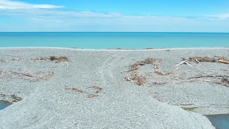 Antena-Baja-Desde-La-Hermosa-Laguna-Rakaia-De-Color-Turquesa-Hasta-El-Océano-Pacífico-Sur-A-Través-De-Grava-Y-Madera-A-La-Deriva