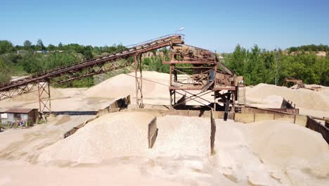 piles of sand and a conveyor belt at an old sand quarry close to the town of prudnik, poland - aerial pullback shot