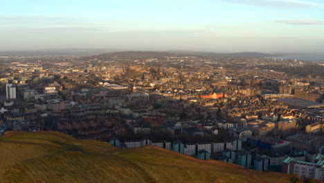 Aerial-view-from-Salisbury-Crags-in-Holyrood-park-to-reveal-Edinburgh-city-as-dawn-breaks,-Scotland