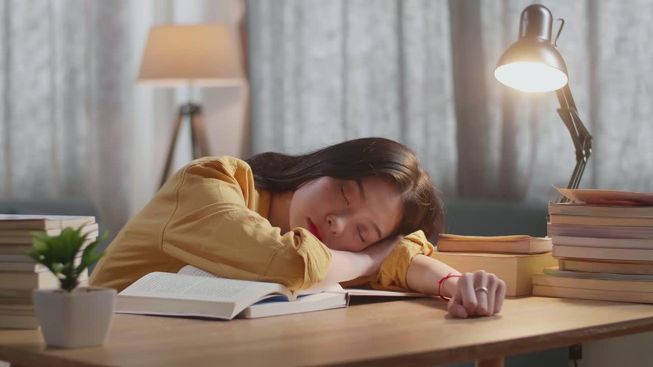 젊은 아시아 여성이 집에서 공부하고 책 위에 책 읽으면서 잠을 자고 있습니다.