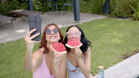 dos amigas biraciales disfrutando de la sandía y tomando selfies en casa