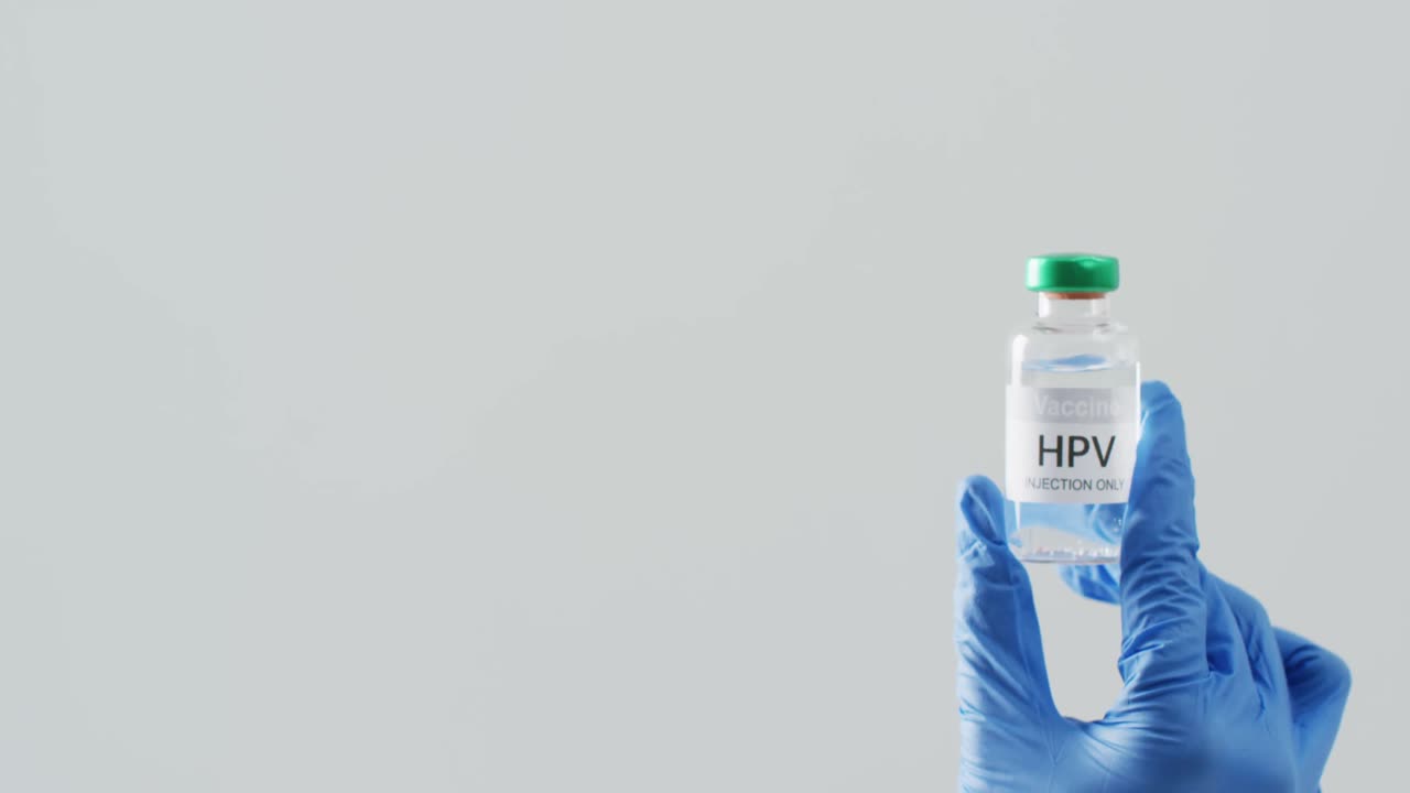 vídeo de la mano con guante quirúrgico sosteniendo el vial de la vacuna contra el vih en un fondo gris con espacio para copiar