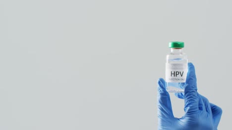 video of hand wearing surgical glove holding hpv vaccine vial on grey background with copy space