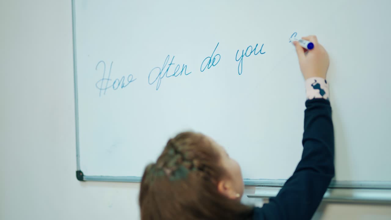 Learning process at school. Little girl writing with a marker on magnetic blackboard. Schoolgirl in the classroom. Elementary education.