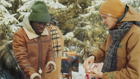 friends grilling sausages at campsite in winter forest