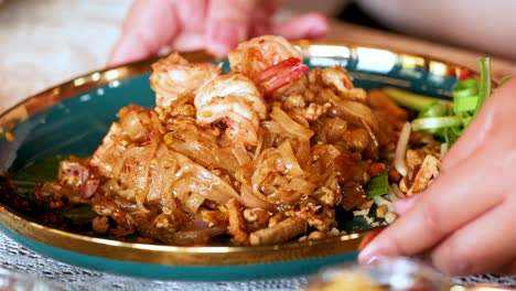 hands presenting shrimp pad thai on a plate