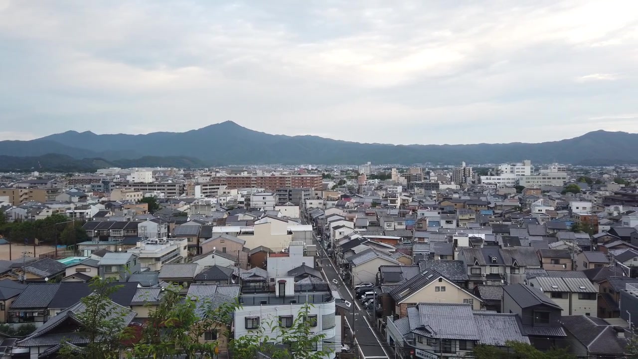 Panoramica aerea di un quartiere residenziale con case storiche a Kyoto, Giappone, paesaggio urbano storico, skyline all'ora blu e sfondo montuoso. Inquadratura di ambientazione.
