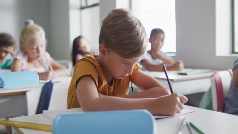 Video-of-focused-caucasian-boy-sitting-at-desk-in-classsroom