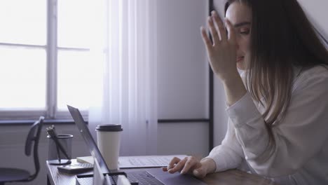 a woman is working with her laptop in an office. she reads something funny and she seems to be happy.