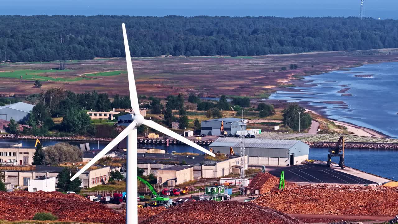 Wind turbine by coastal industry during daytime, symbolizing clean energy