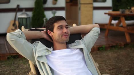 pleased, handsome caucasian man chilling out while laying on summer bed outdoors. traveling, rest, vacation concept. trailer, wheels house on the blurred background