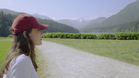 a young woman wearing a baseball cap looks toward the majestic mountains in the background, then turns and smiles at the camera