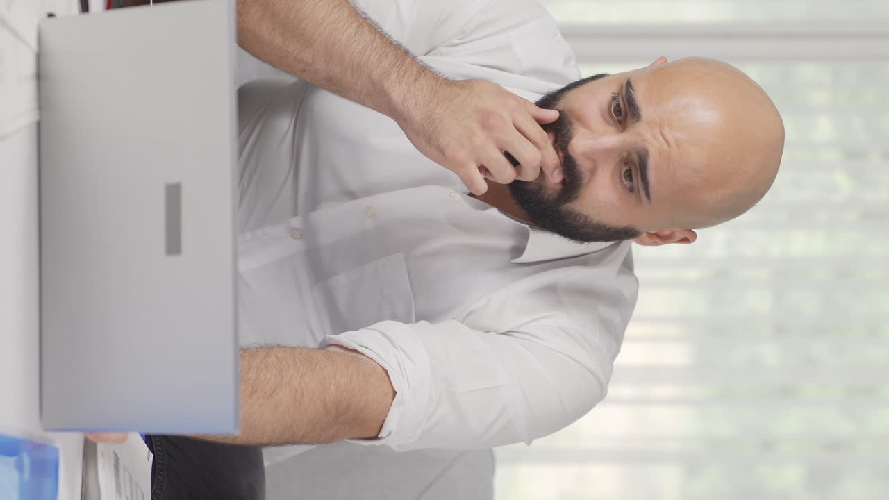 Vertical video of Home office worker man working on laptop stressed.