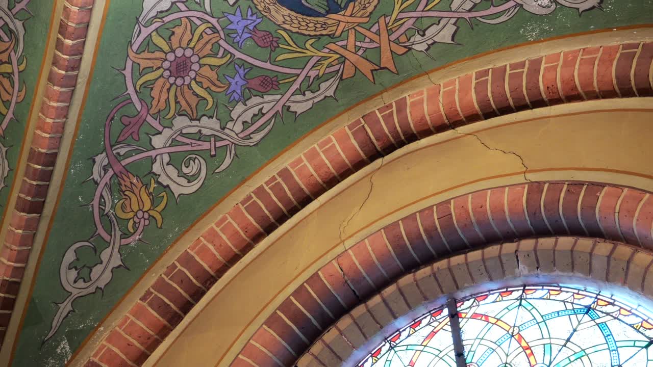 Ruinas de iglesia histórica con murales religiosos desvanecidos y grieta estructural.