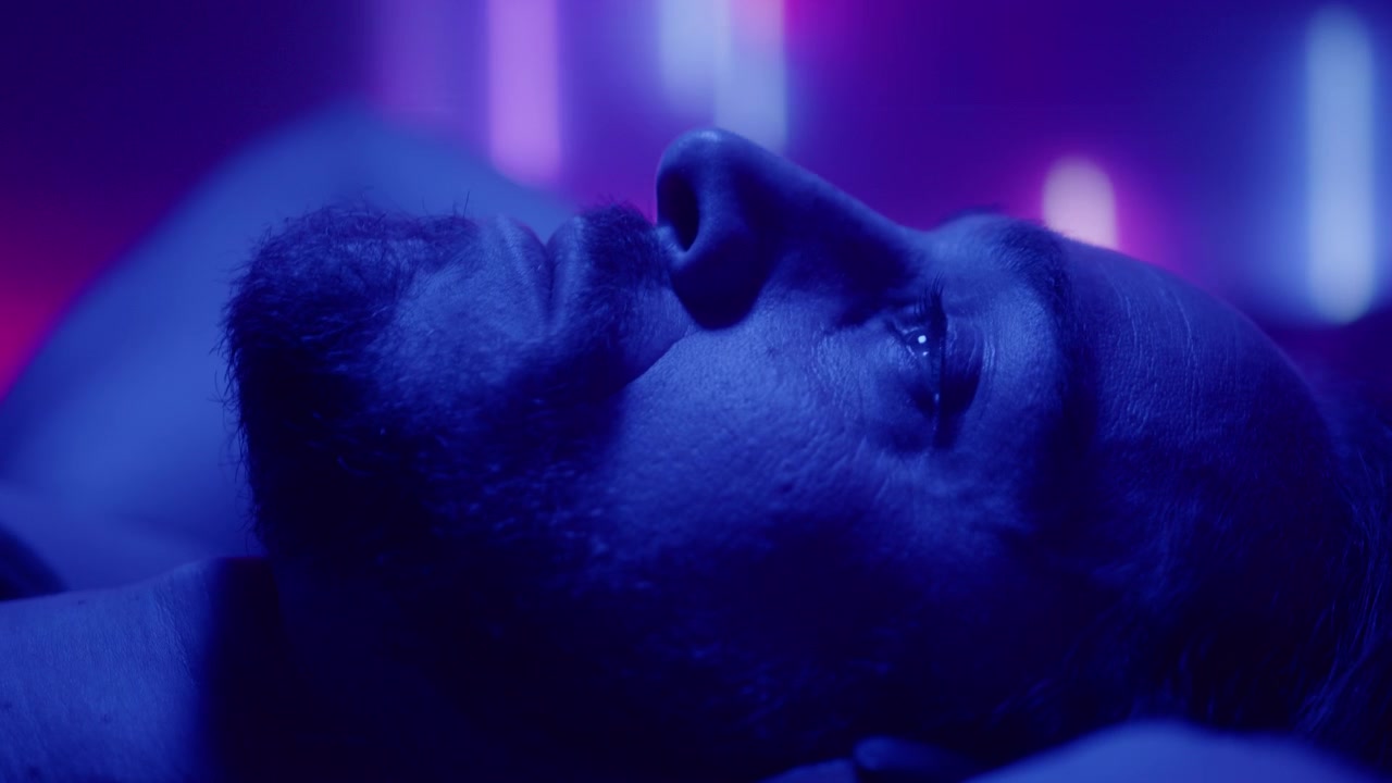 Depressed Man in Headphones Lying Down in Room with Neon Light