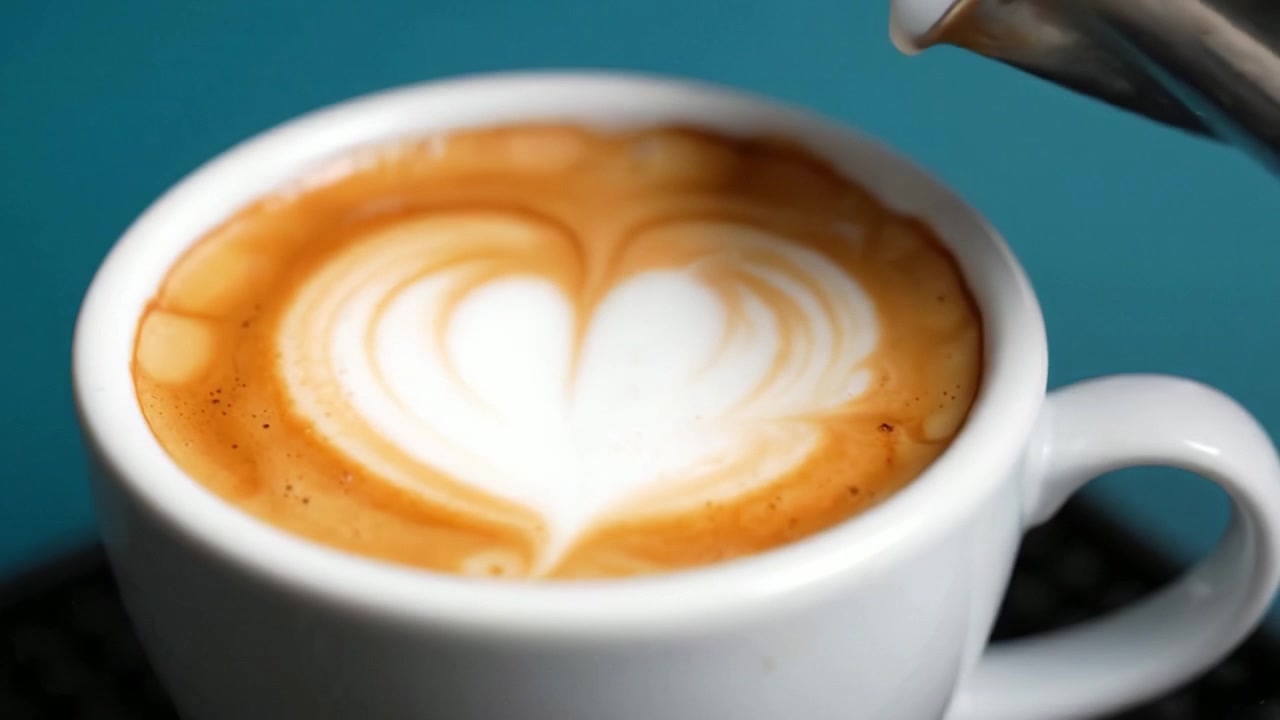 Un latte macchiato splendidamente preparato con arte in schiuma a forma di cuore in una tazza di ceramica bianca su uno sfondo vivace che celebra l'arte della preparazione e del piacere del caffè