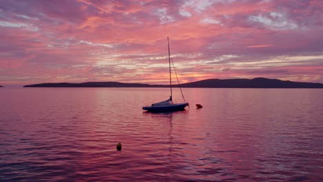 Small-sailboat-anchored-at-coast-of-Brodarica-Croatia-with-amazing-sunset,-aerial