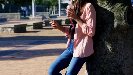 woman using mobile phone while having juice in park 4k