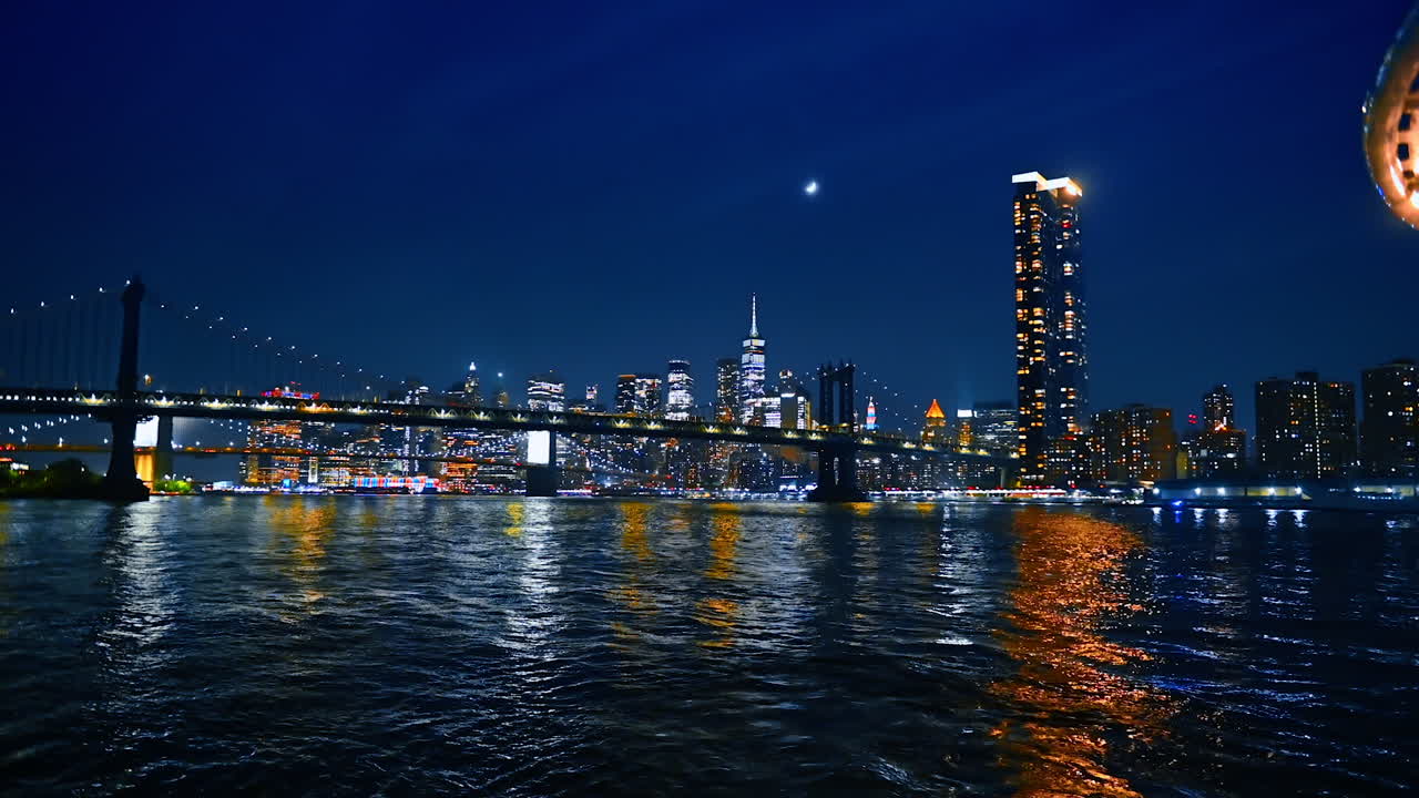 Lights of amazing New York reflect in the dark waterscape of the East River. Low angle view at the Manhattan Bridge and city skyline from the river at night