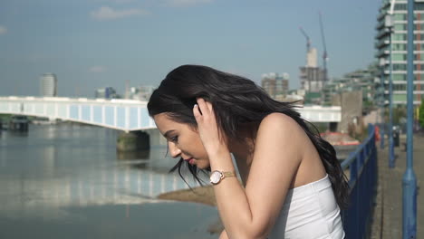 beautiful latina woman on holiday leaning against the railing, looking down at the river thames in london