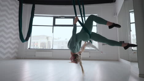 dos jóvenes mujeres yogi practicando yoga aéreo en hamacas verdes en un club de fitness. hermosas mujeres trabajando en clase realizando aero yoga. variación de la postura de la pirámide parsvottanasana