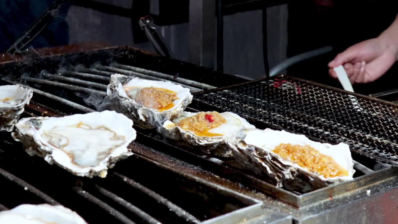 Close-up of oysters being seasoned with garlic sauce on a grill, highlighting the cooking process.