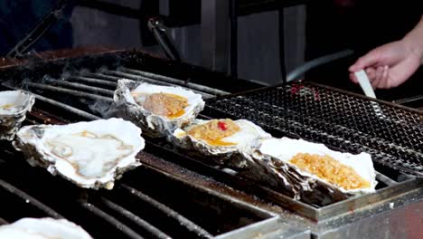 close-up of oysters being seasoned with garlic sauce on a grill, highlighting the cooking process.