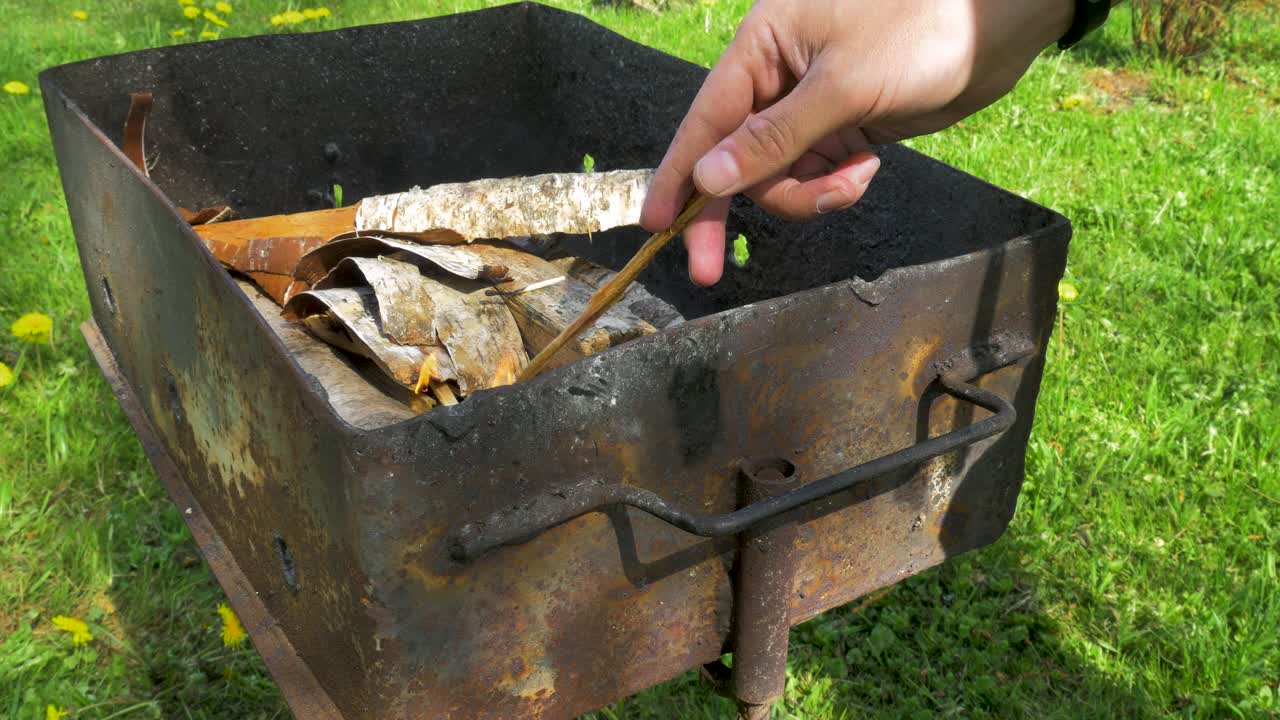 청년은 장작을 태우고 베이킹과 바비큐를 위해 녹슨 그릴을 준비하고, 중간 클로즈업 샷