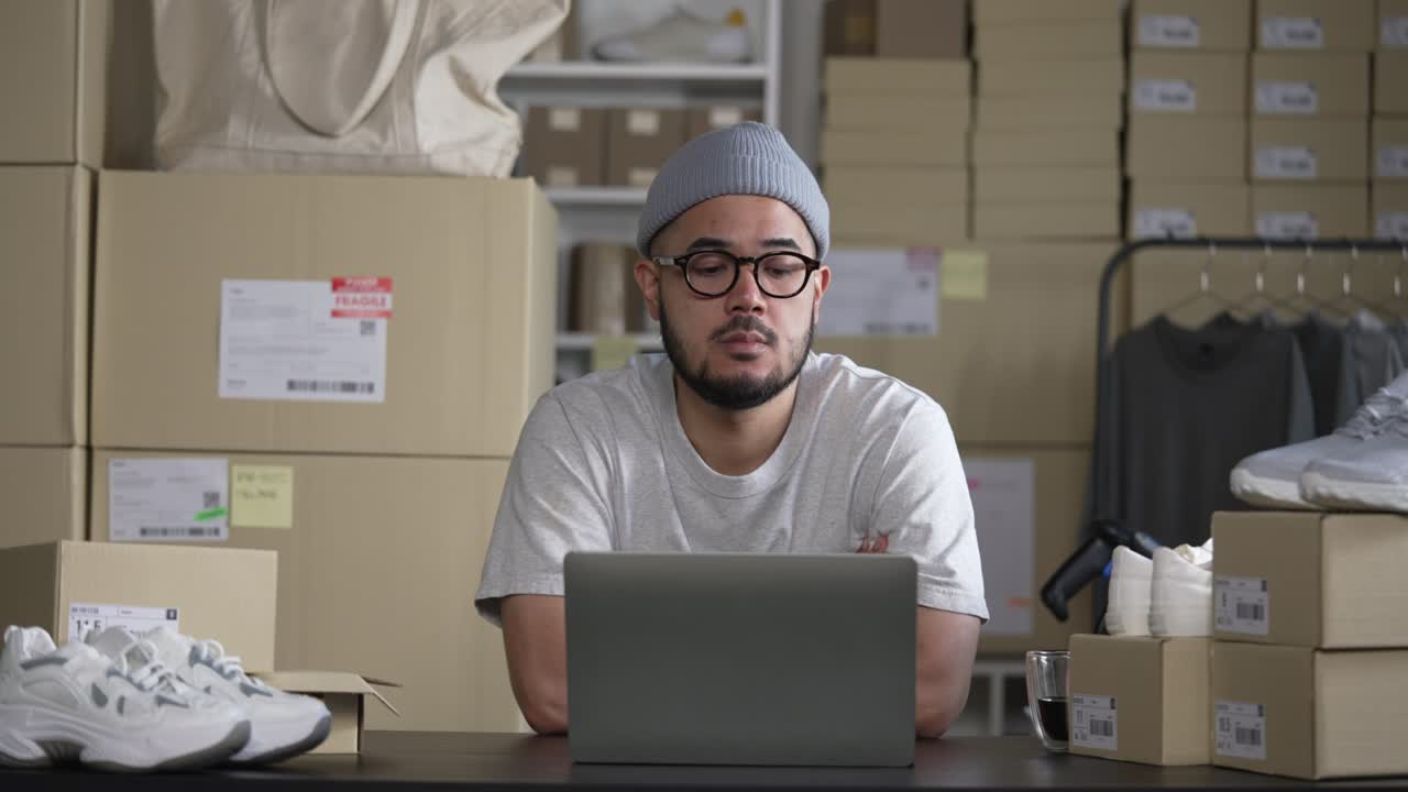 emprendedor vendedor en línea en un almacén mirando una computadora portátil y preocupándose por el negocio de comercio electrónico debido a la falta de ventas y clientes.