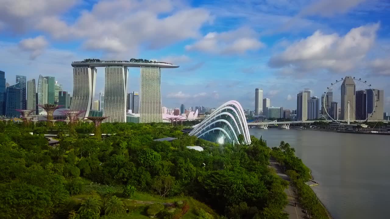 Aerial drone shot flying forward, showcasing Marina Bay Sands, Gardens by the Bay, and the Flower Dome with Singapore’s urban skyline in the background