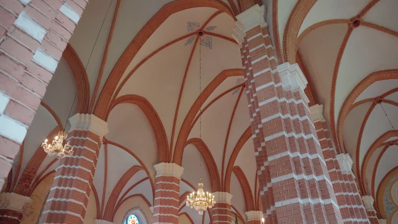 Captivating view of a Gothic cathedral's intricate vaulted ceiling with arched brick designs and elegant chandeliers, highlighting the serene, historic ambiance of this sacred space