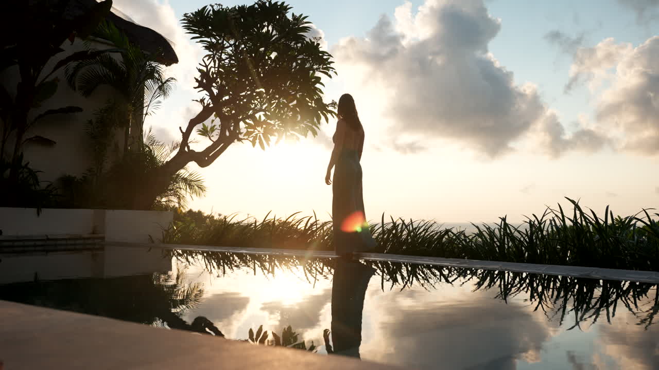 silueta de una mujer caminando por el borde de la piscina al amanecer en un complejo de lujo