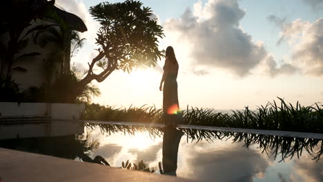 Silhouette-of-woman-walking-on-pool-edge-at-sunrise-at-luxury-resort