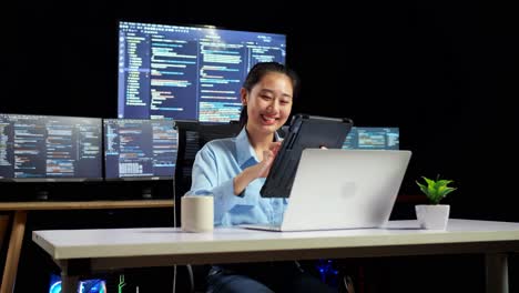 asian female programmer using tablet while writing code by a laptop using multiple monitors showing database on terminal window desktops in the office