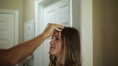 slow motion shot of a young girl standing against a wall having her height measured by her parent