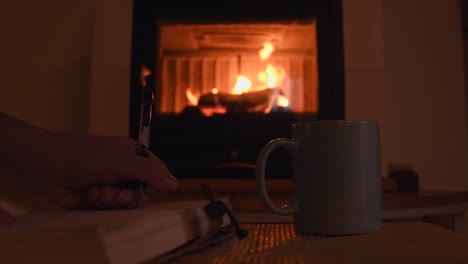 cozy background of a young female hand writing on a old notebook near a warm fireplace, with a cup with hot steam getting out of it