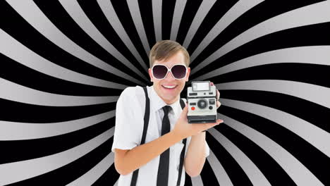 retrato de un hombre caucásico sosteniendo una cámara polaroid contra un fondo radial negro y gris
