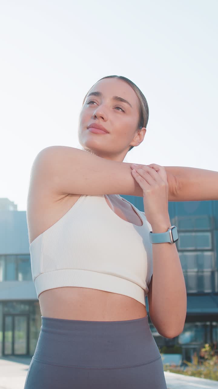 Caucasian sporty young woman runner stretching arms warm up before jogging in city park on sunny day