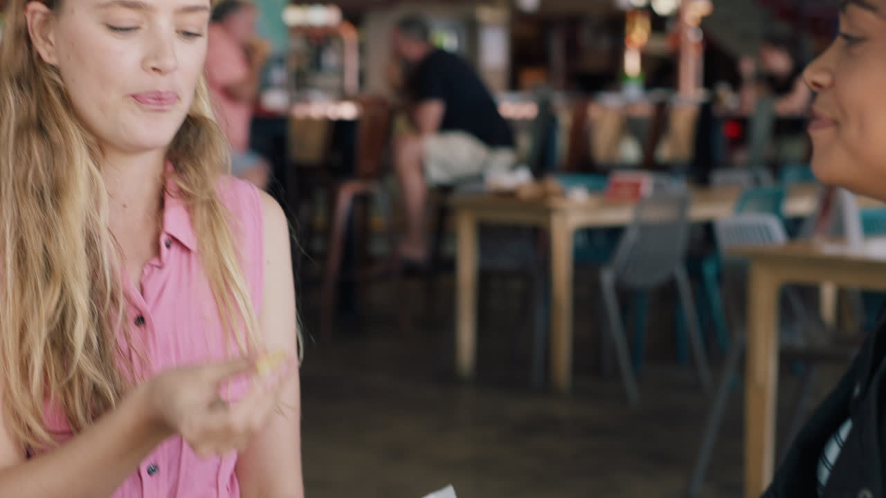 웃긴 여성이 입으로 음식을 잡고 레스토랑에서 가장 친한 친구가 게임을 하고 친구가  ⁇ 김을 던지고 두 여성이 즐겁게 놀고 있습니다.