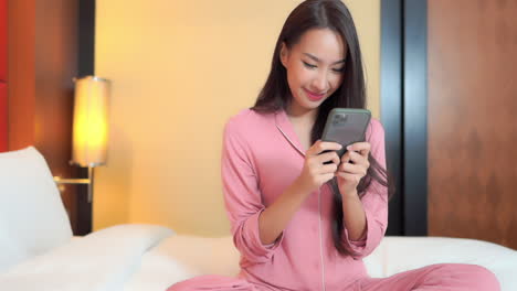 Adult-Woman-in-Pajamas-Sitting-on-Bed-Using-Smartphone,-Texting-SLOMO