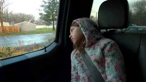 young girl sitting in back seat of car looking through window with sad, depressed mood