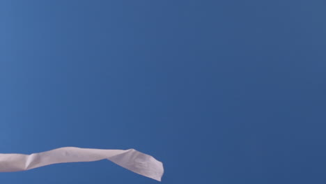 a toilet paper roll is seen flying through the air slowly in front of a blue backdrop