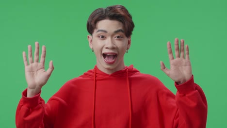 portrait of a young asian transgender male opening her eyes with palms and becoming surprised in the green screen studio