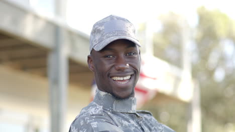 happy african american male soldier laughing with flag in background on sunny day, slow motion